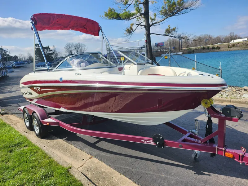 Slide: The Image of 2013 Tahoe Q7i boat with red and white design on a trailer by a lake. - 8