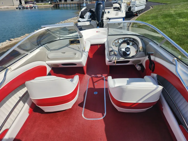 Slide: The Image of 1997 Bayliner 2050 Capri SS boat interior with red and white seating, docked by the water. - 10