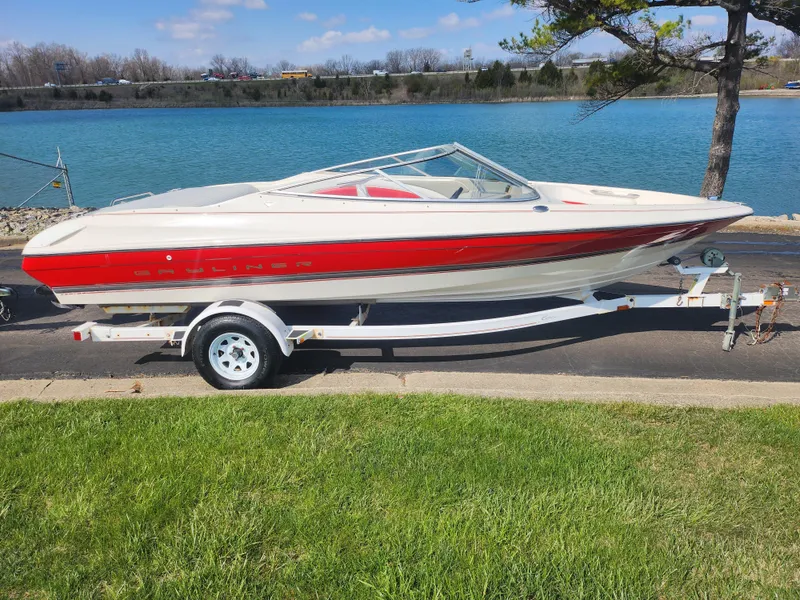 Slide: The Image of 1997 Bayliner 2050 Capri SS boat on trailer by a lake, featuring red and white design. - 9