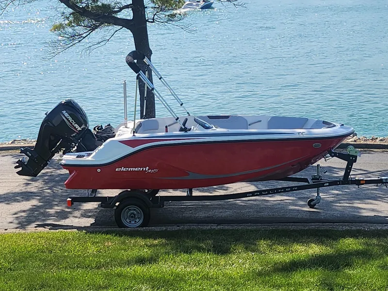 Slide: The Image of 2023 Bayliner Element M15 boat on trailer by a lake, red and white design. - 0