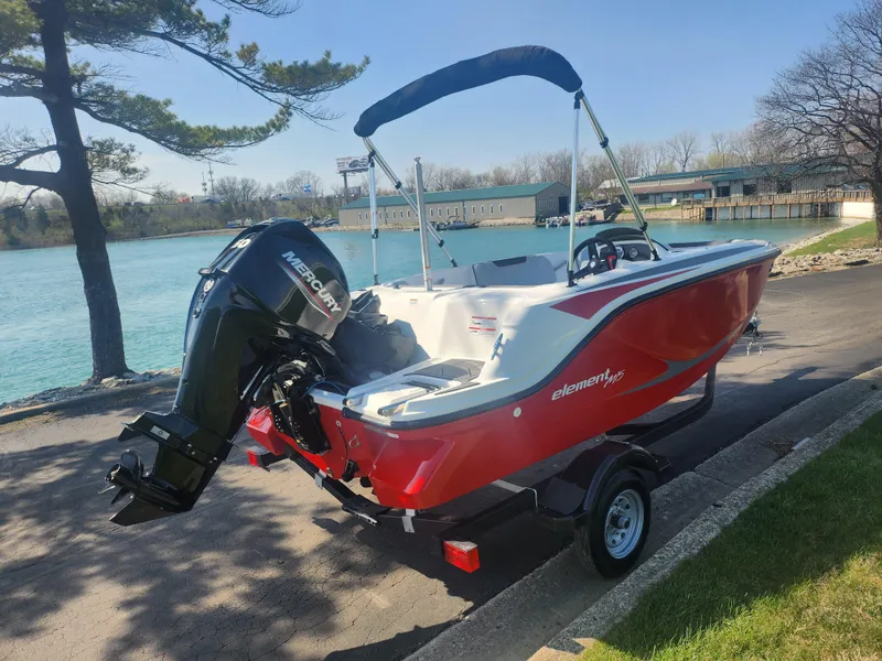 Slide: The Image of 2023 Bayliner Element M15 boat with Mercury outboard motor, parked by a scenic lake. - 1