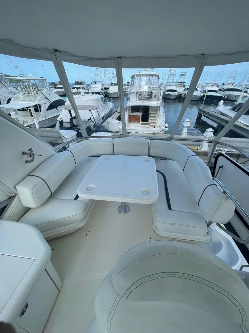 Slide: The Image of 2006 Sea Ray 44 Sedan Bridge yacht interior with white seating and table, docked at marina. - 18