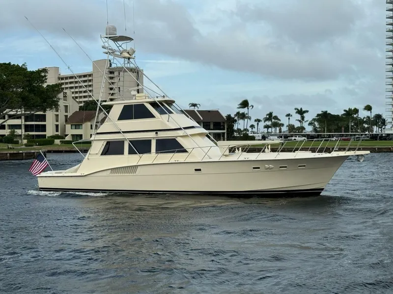 The Image of 1985 Hatteras Enclosed Bridge yacht cruising on a waterway near modern buildings. - 1