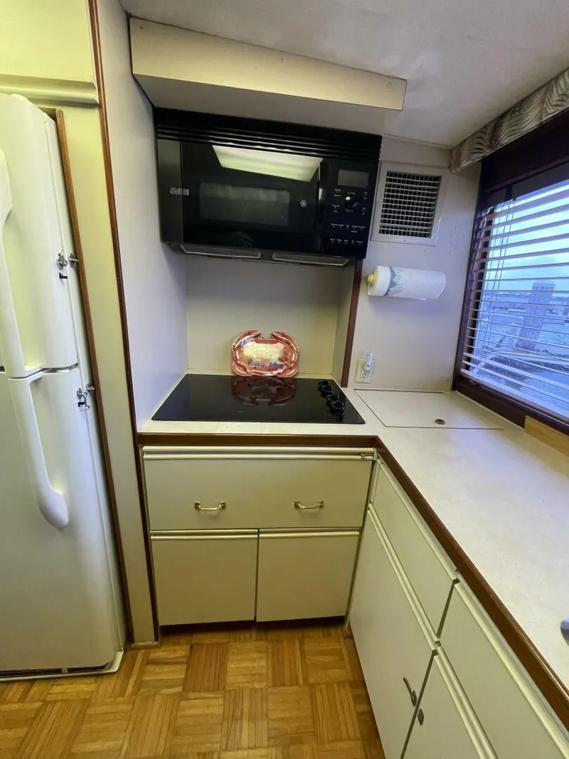 Slide: The Image of 1985 Hatteras Enclosed Bridge kitchen with stove, microwave, and refrigerator. - 10