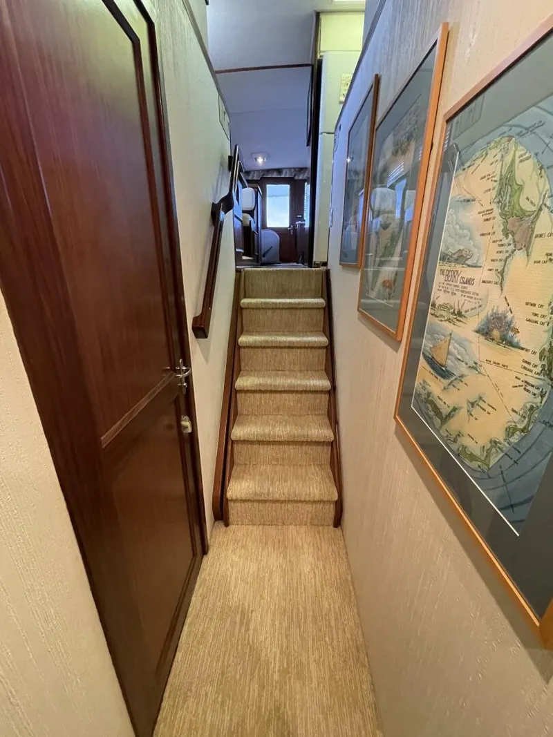 Slide: The Image of Narrow hallway with stairs in a 1985 Hatteras Enclosed Bridge yacht, featuring framed maps. - 12