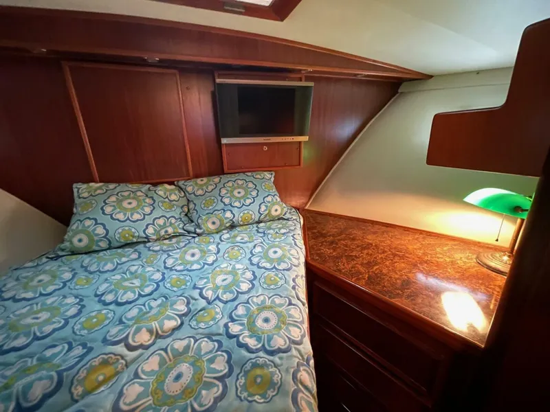 Slide: The Image of 1985 Hatteras Enclosed Bridge cabin with floral bedding, wood paneling, and a small TV. - 18