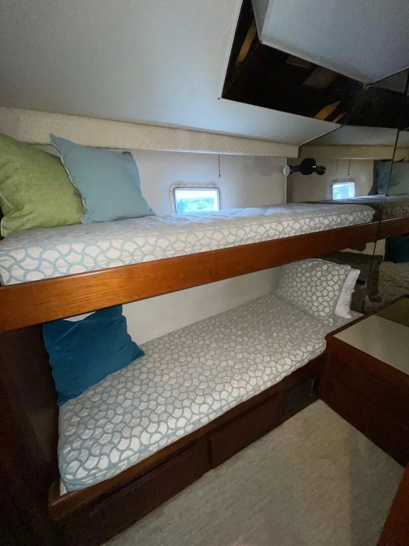 Slide: The Image of 1985 Hatteras Enclosed Bridge cabin with bunk beds, cozy bedding, and small windows. - 21