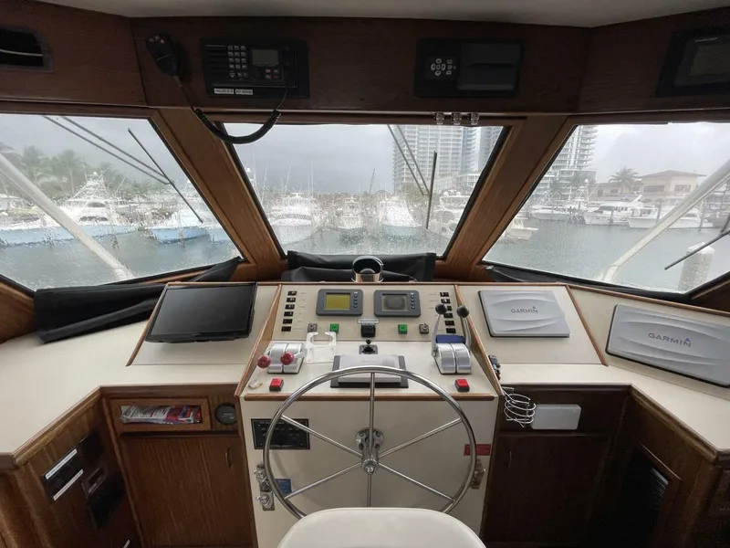 Slide: The Image of 1985 Hatteras Enclosed Bridge helm with navigation equipment and marina view. - 25