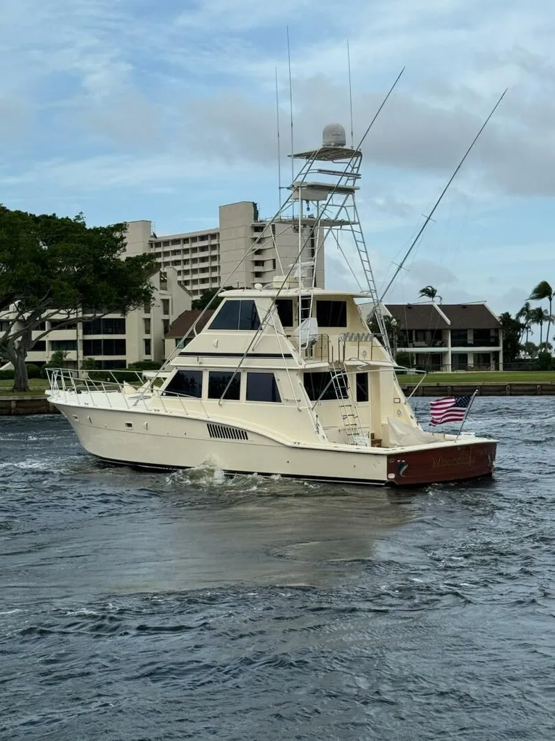 Slide: The Image of 1985 Hatteras Enclosed Bridge yacht cruising near waterfront buildings, with American flag displayed. - 31