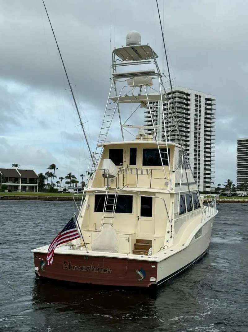 Slide: The Image of 1985 Hatteras Enclosed Bridge yacht on water, with American flag, against cloudy sky and buildings. - 33