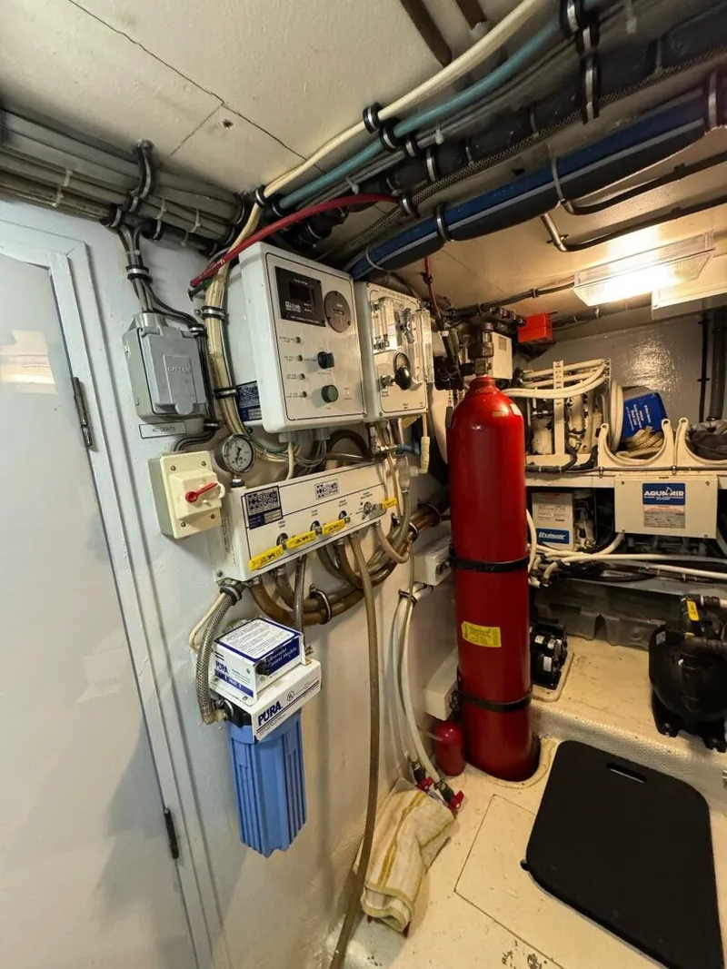 Slide: The Image of Engine room of 1985 Hatteras Enclosed Bridge yacht with control panels and fire extinguisher. - 48