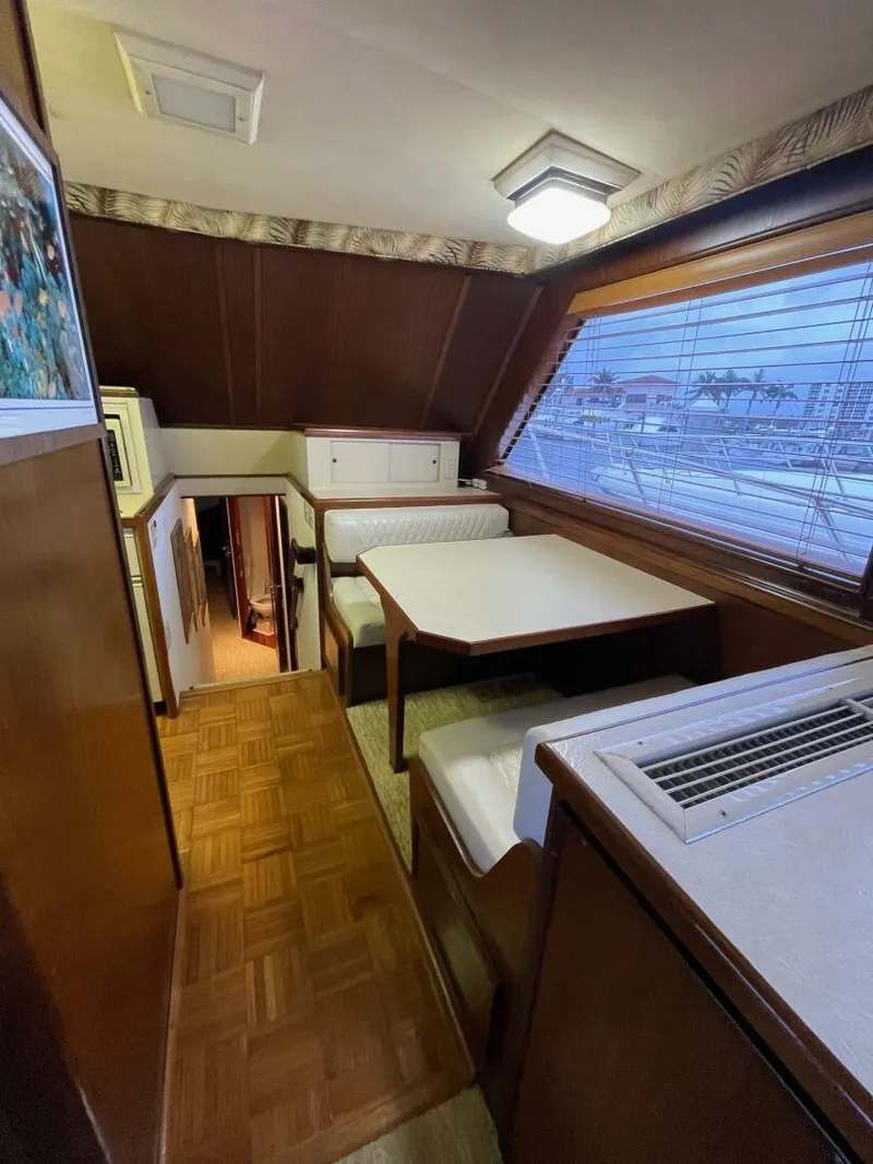 Slide: The Image of 1985 Hatteras Enclosed Bridge interior with dining area, wood paneling, and large window. - 7