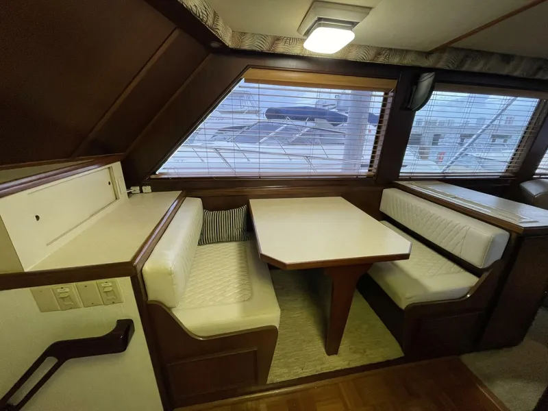 Slide: The Image of 1985 Hatteras Enclosed Bridge interior with dining area, featuring white cushioned seating and wooden table. - 8
