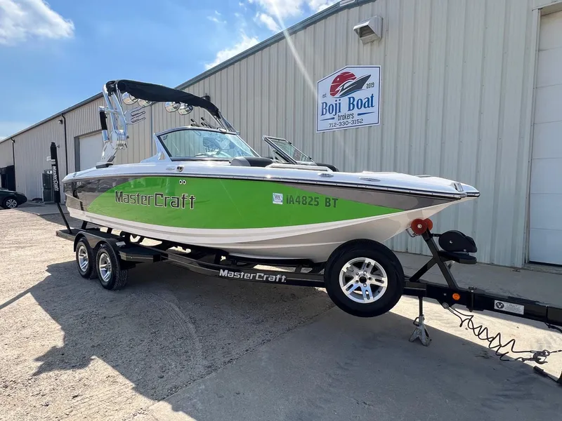 Slide: The Image of 2013 MasterCraft X-25 boat with green detailing on a trailer outside Boji Boat Brokers. - 1