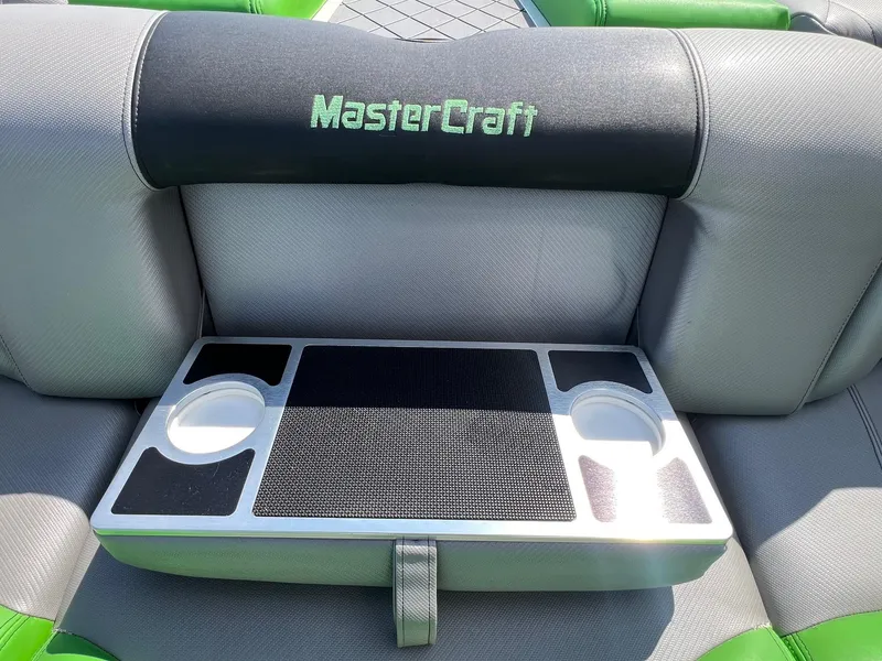 Slide: The Image of 2013 MasterCraft X-25 boat seat with cup holders and tray, featuring green and gray upholstery. - 36