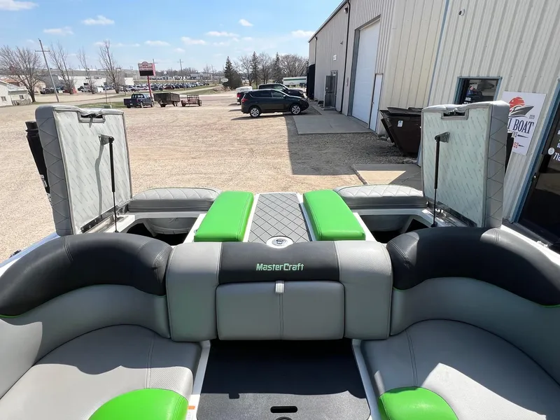 Slide: The Image of 2013 MasterCraft X-25 boat interior with green and gray seating, parked outside a building. - 43