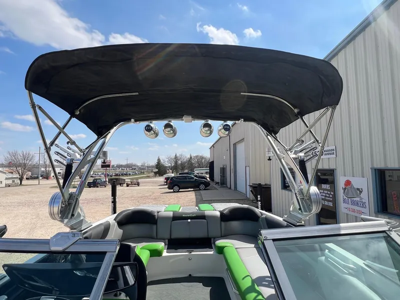 Slide: The Image of 2013 MasterCraft X-25 boat with black canopy and green-accented seating, parked outdoors. - 46