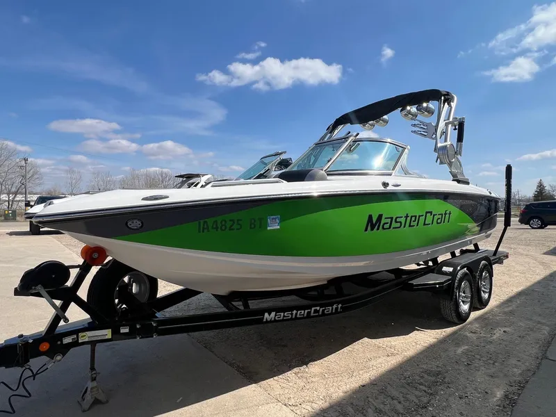 Slide: The Image of 2013 MasterCraft X-25 boat with green accents on a trailer under a clear blue sky. - 5