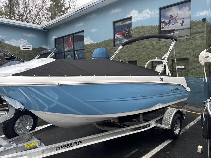 Slide: The Image of 2025 Stingray 172 SC boat in blue on a trailer, parked outside a building. - 0