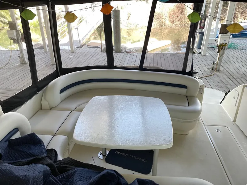 Slide: The Image of 2004 Sea Ray 420 Sundancer interior with curved seating and table, dockside view. - 10