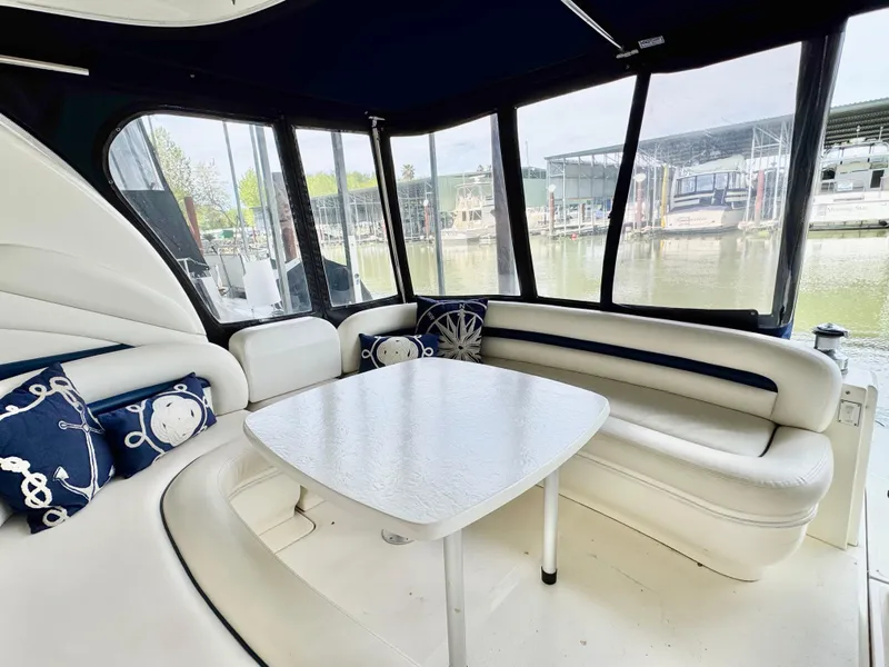Slide: The Image of 2004 Sea Ray 420 Sundancer interior with white seating, nautical pillows, and waterfront view. - 9