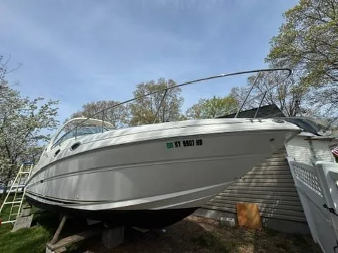 Slide: The Image of 2003 Sea Ray 280 Sundancer boat on land, surrounded by trees and a fence. - 2