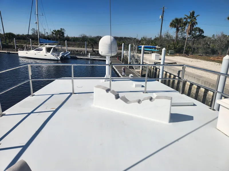 Slide: The Image of 1983 Custom 76 Trawler docked, featuring a spacious deck with railing and clear blue sky. - 10