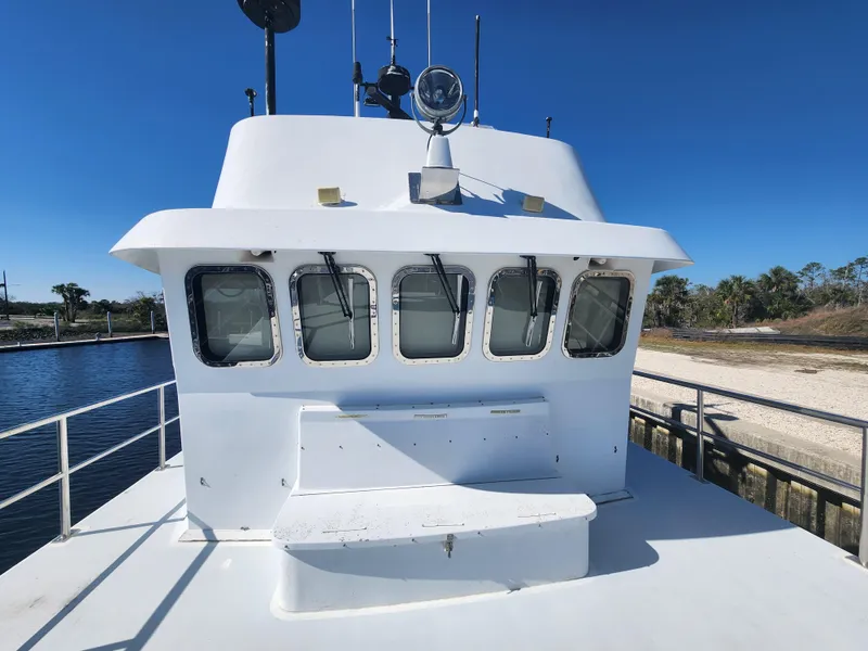 Slide: The Image of 1983 Custom 76 Trawler with white exterior, docked by a calm waterway under clear blue skies. - 12