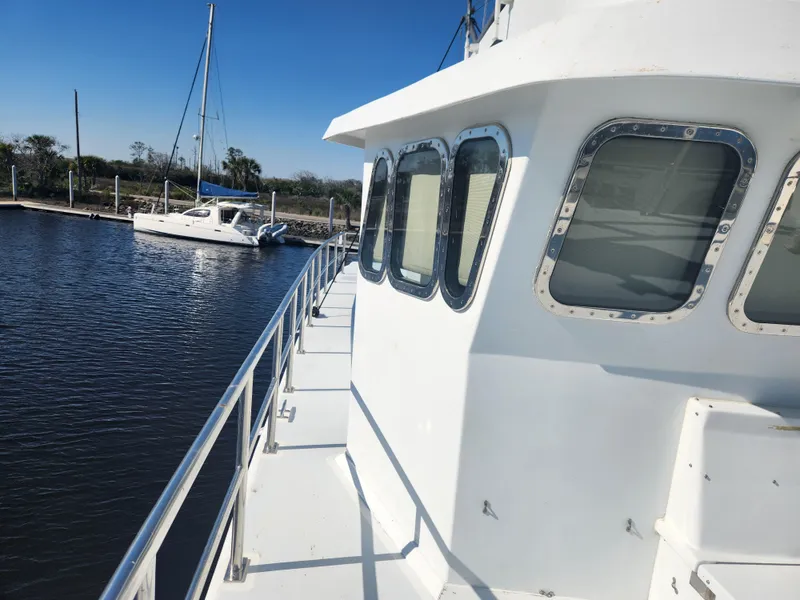 Slide: The Image of 1983 Custom 76 Trawler docked, featuring white exterior and windows, with sailboat in background. - 15