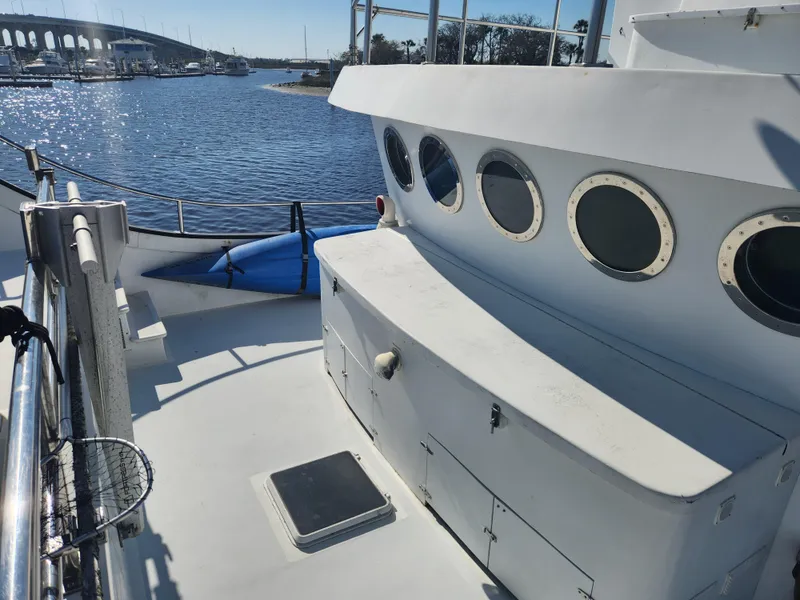 Slide: The Image of 1983 Custom 76 Trawler deck with portholes, docked near a bridge on a sunny day. - 18