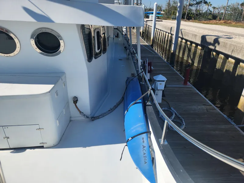 Slide: The Image of 1983 Custom 76 Trawler docked, featuring portholes and a blue kayak on deck. - 19