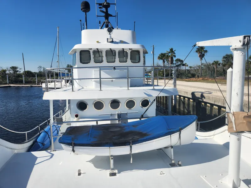 Slide: The Image of 1983 Custom 76 Trawler docked, featuring upper deck and lifeboat under clear blue sky. - 23