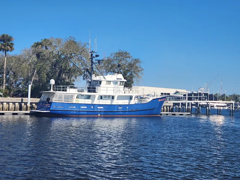 Slide: The Image of Blue 1983 Custom 76 Trawler docked by trees and pier under clear sky. - 5