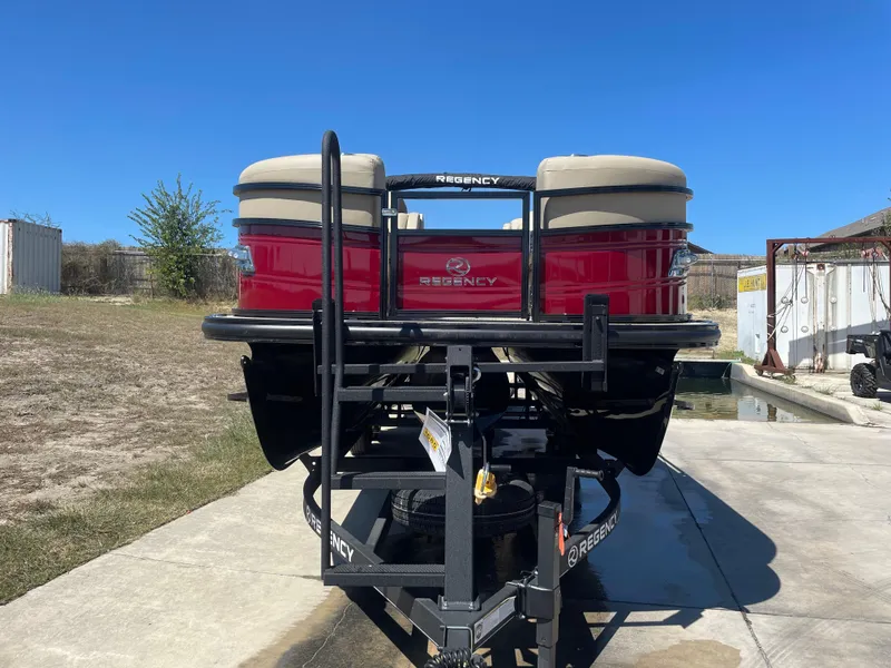 Slide: The Image of 2024 Regency 230 LE3 Sport pontoon boat on trailer, red exterior, parked outdoors. - 6