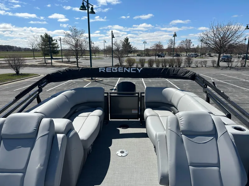 Slide: The Image of 2024 Regency 230 DL3 pontoon boat with spacious seating, parked in an empty lot under a clear sky. - 3