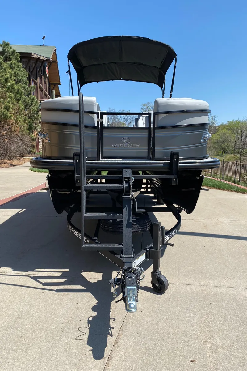 Slide: The Image of 2024 Regency 230 DL3 pontoon boat on trailer, parked on a sunny driveway. - 2