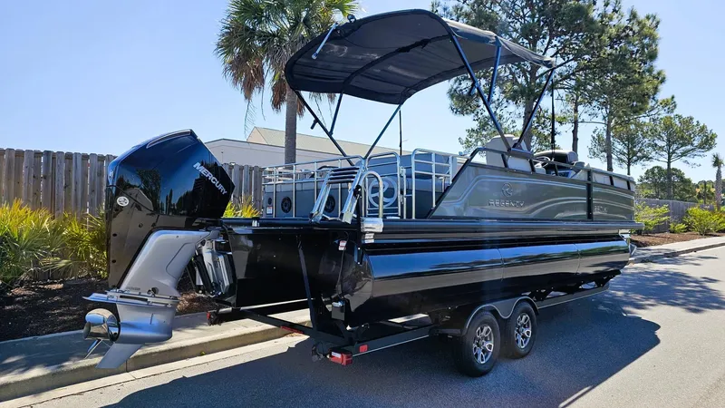 Slide: The Image of 2024 Regency 230 LE3 Sport pontoon boat on trailer, parked outdoors. - 2