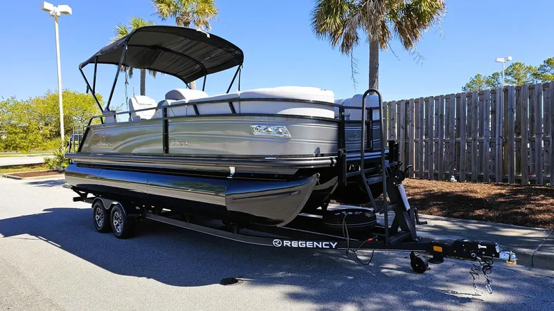 Slide: The Image of 2024 Regency 230 LE3 Sport pontoon boat on trailer, parked outdoors. - 3