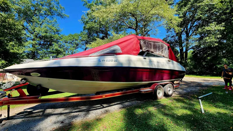 Slide: The Image of 1996 Crownline 266 BR boat with red cover on a trailer, surrounded by trees. - 3
