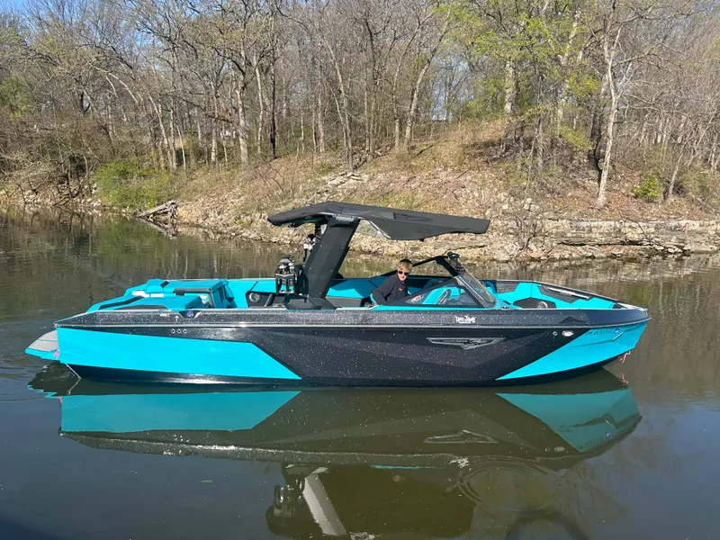 Slide: The Image of 2023 Nautique Super Air Nautique S25 boat on a calm lake with wooded background. - 2