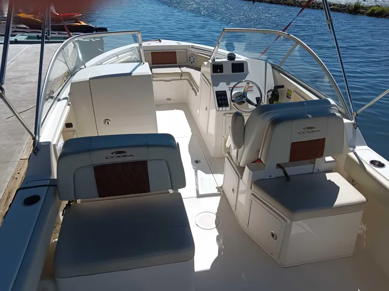 Slide: The Image of 2021 Cobia 220 Dual Console boat interior with seating and steering, docked by the water. - 0
