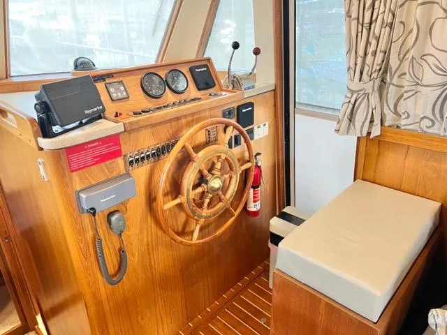 Slide: The Image of 2002 Mainship 390 Trawler helm with wooden wheel, navigation instruments, and cushioned seating. - 26
