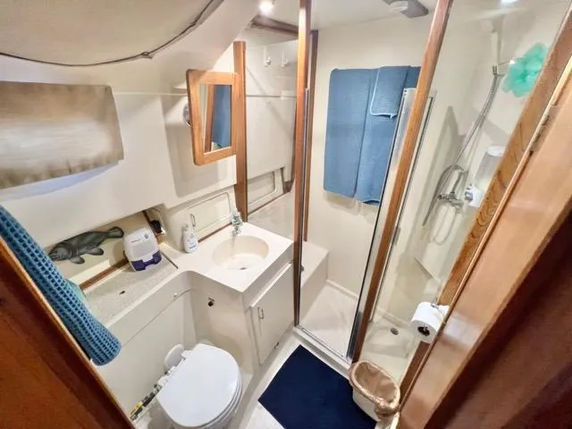 Slide: The Image of 2002 Mainship 390 Trawler bathroom with shower, sink, and toilet, featuring wooden accents. - 33