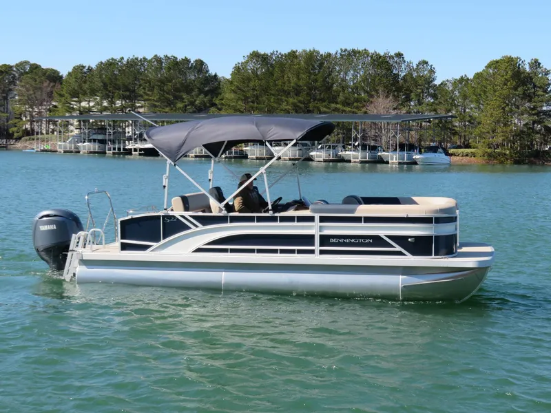 Slide: The Image of 2025 Bennington 22SSB pontoon boat on a serene lake with lush green trees. - 22
