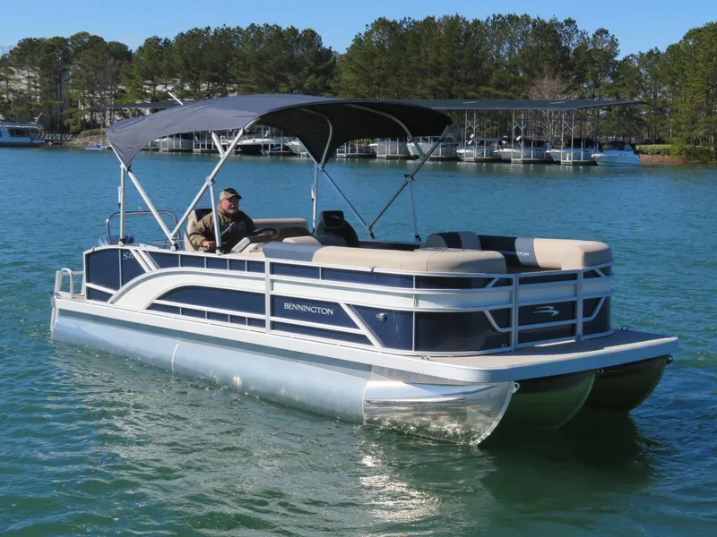 Slide: The Image of 2025 Bennington 22SSB pontoon boat cruising on a lake with canopy and seating. - 25