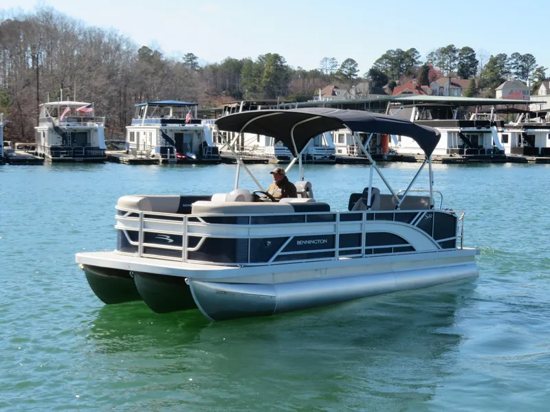 Slide: The Image of 2025 Bennington 22SSB pontoon boat cruising on a lake with docks in the background. - 26