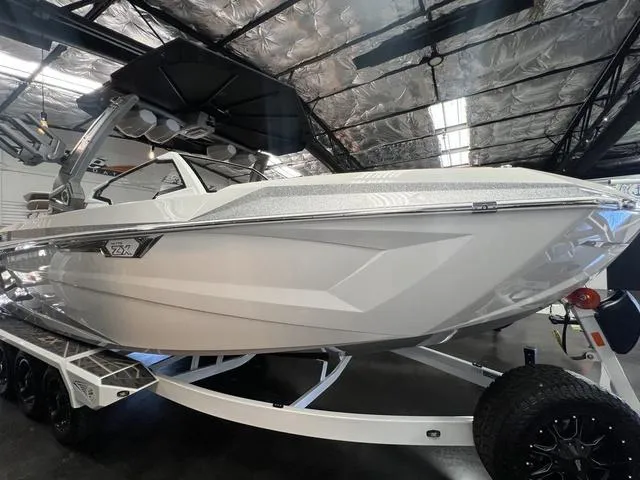 Slide: The Image of 2025 Tigé 25ZX boat in showroom, sleek design, white exterior, on trailer. - 1