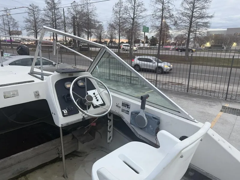 Slide: The Image of 1977 Boston Whaler 21 REVENGE boat cockpit with steering wheel and controls, parked near a road. - 13