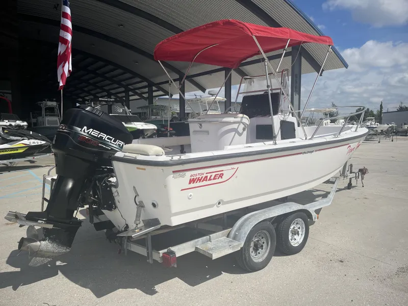 Slide: The Image of 1997 Boston Whaler 21 Outrage boat with red canopy on trailer, parked outdoors. - 2