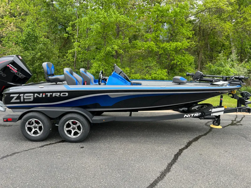 The Image of 2025 Nitro Z19 Pro boat on trailer, parked on asphalt with green trees in background. - 0